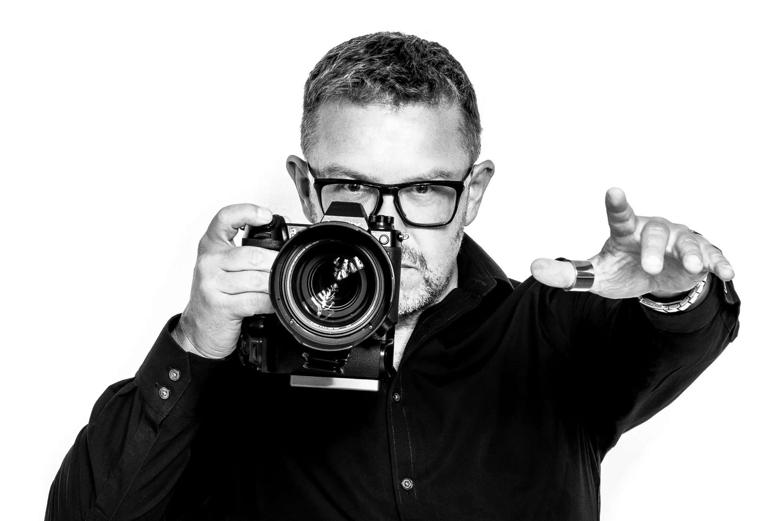 Jens Achtert, Fotograf und Regisseur, mit Kamera am Auge vor hellem Studiohintergrund