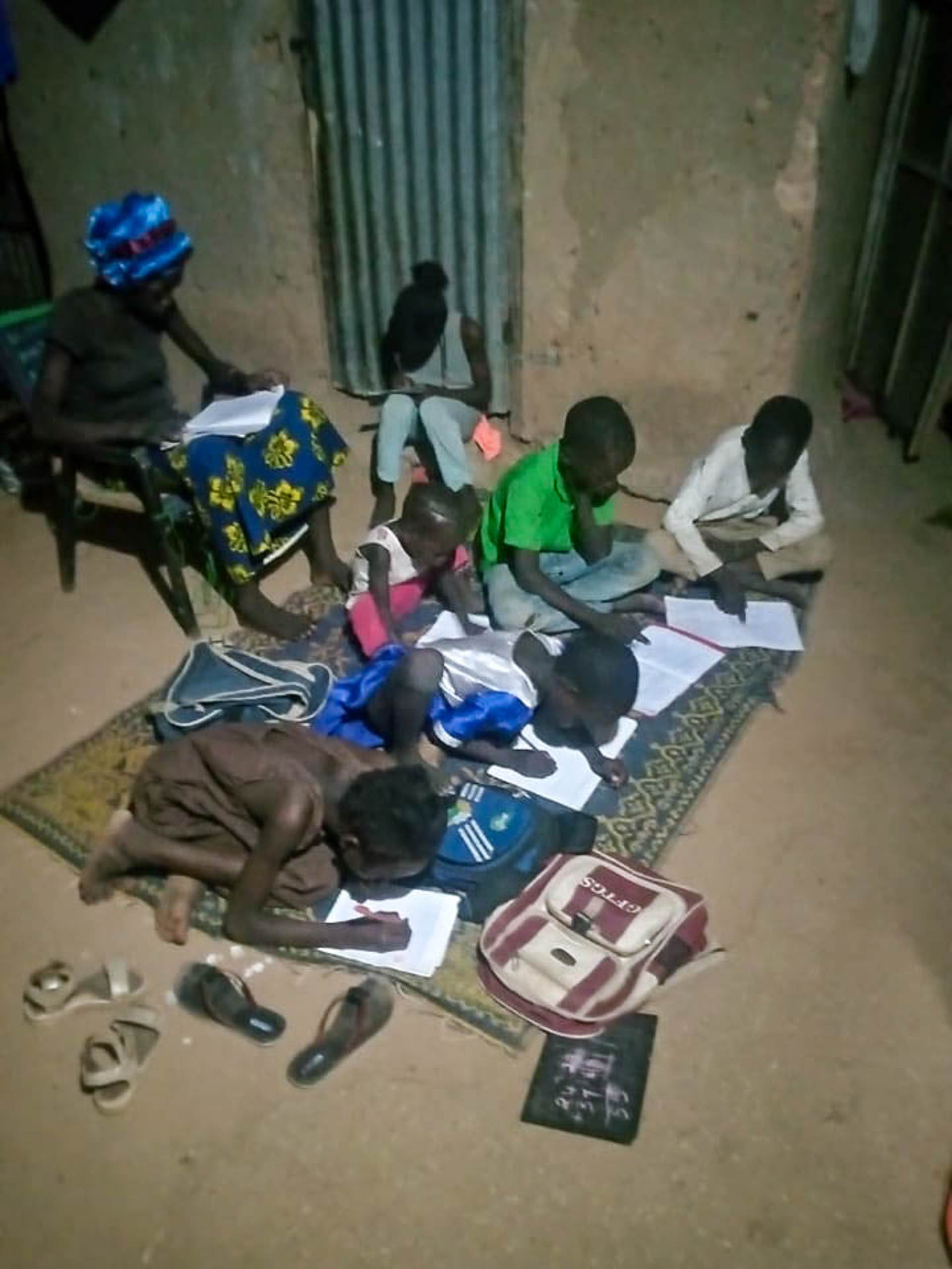 Kinder machen abends auf einer Matte ihre Hausaufgaben, mit Schulranzen, Heften und Tafel, Zinder, Niger · Projekt #waterforzinder