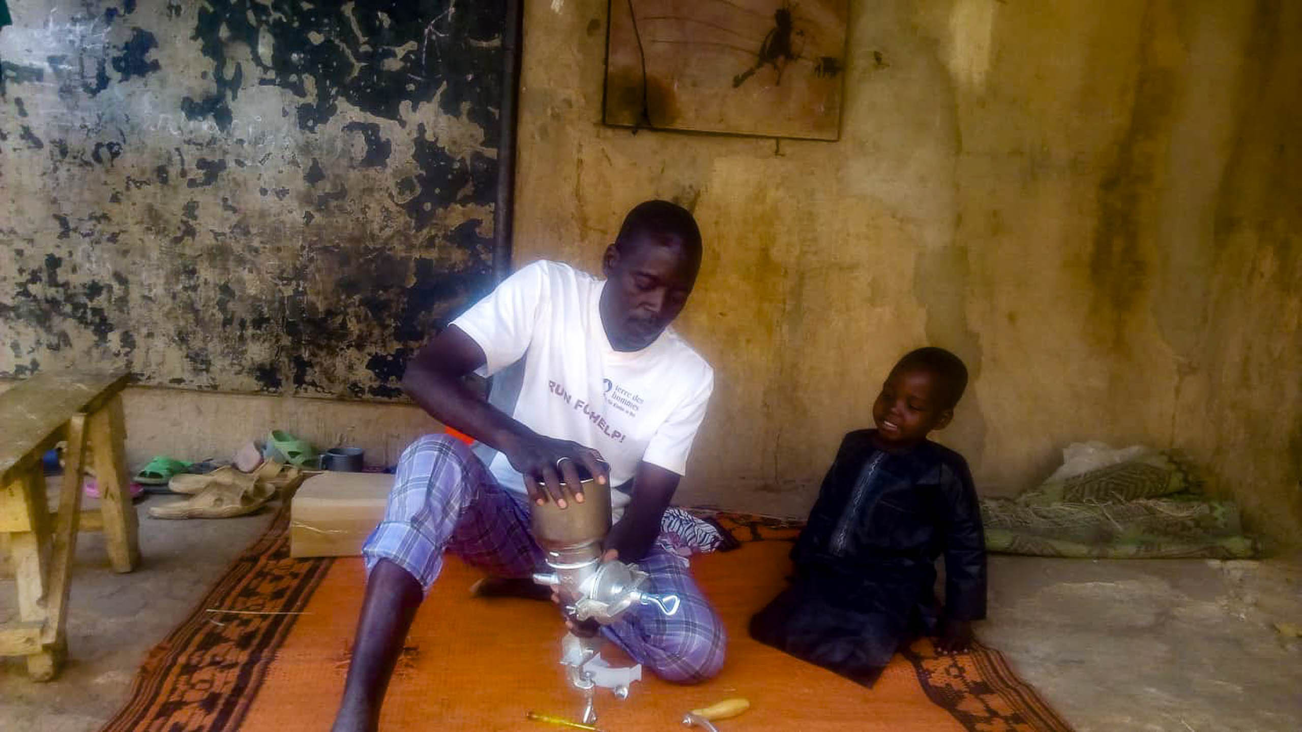 Mourtala Issa montiert eine gespendete Handmuehle, ein Kind sieht zu, Zinder, Niger