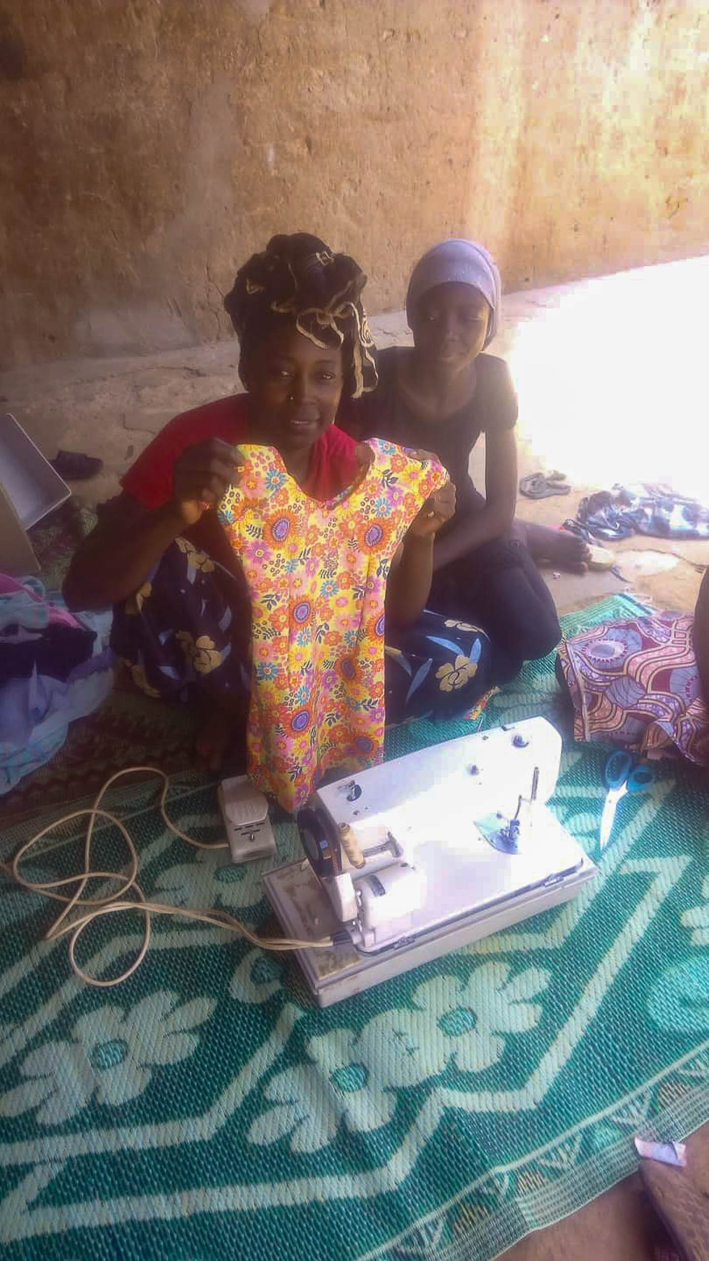 Frau zeigt stolz ein selbstgenaehtes Kleid an der gespendeten Naehmaschine in Zinder, Niger