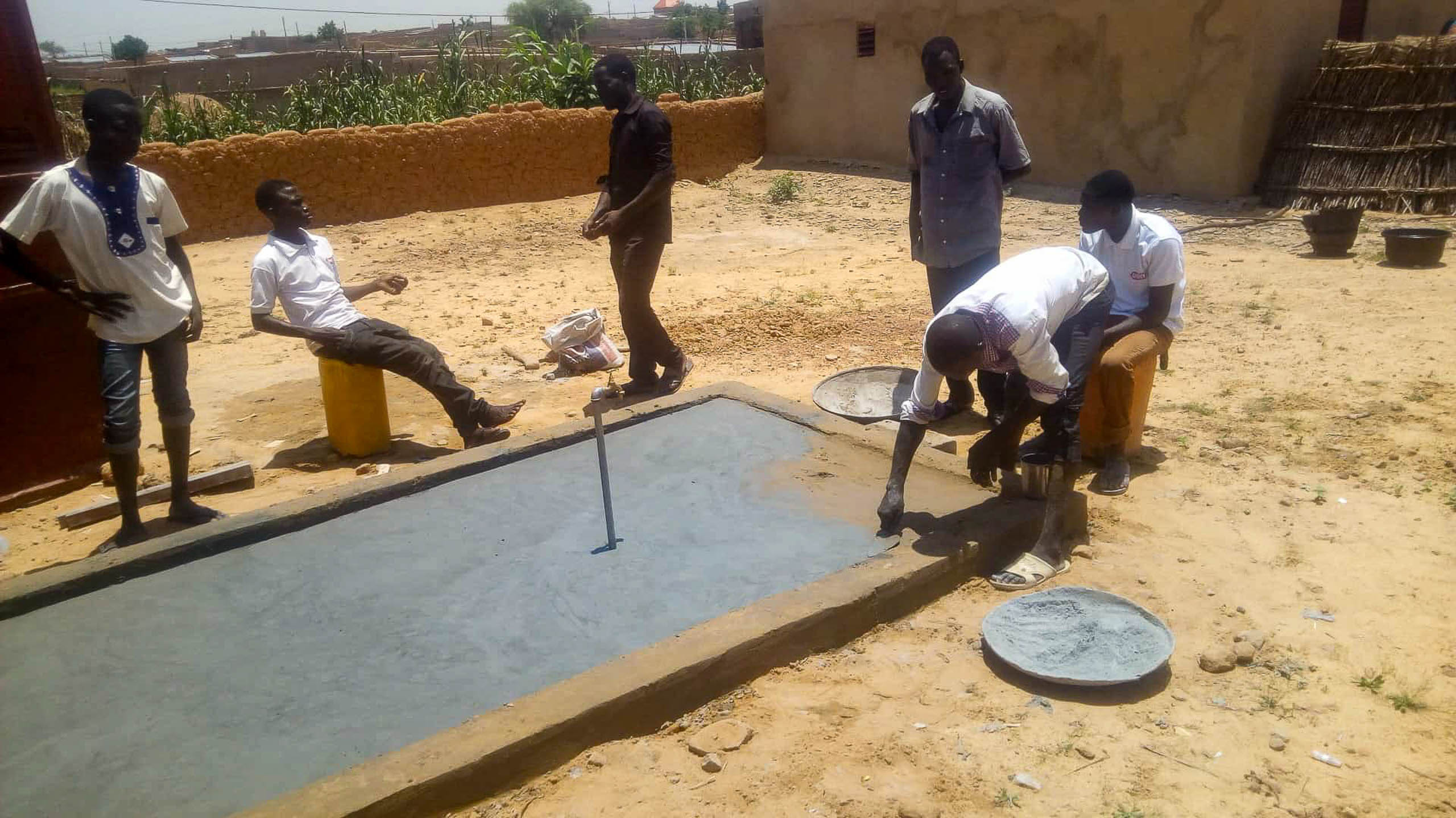 Anschluss der Wasserleitung an das Netz: Wasseruhr und Ventile an der Lehmwand, Maenner arbeiten im Graben, Zinder, Niger