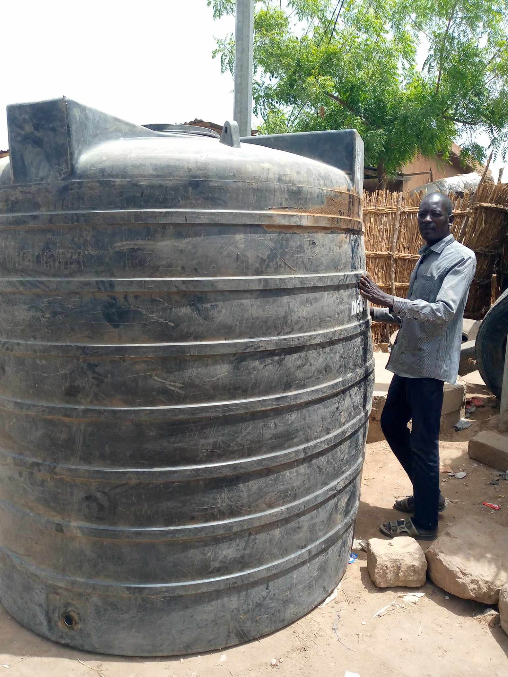 Mourtala Issa steht am fertig installierten grossen Wassertank in Zinder, Niger · Projekt #waterforzinder