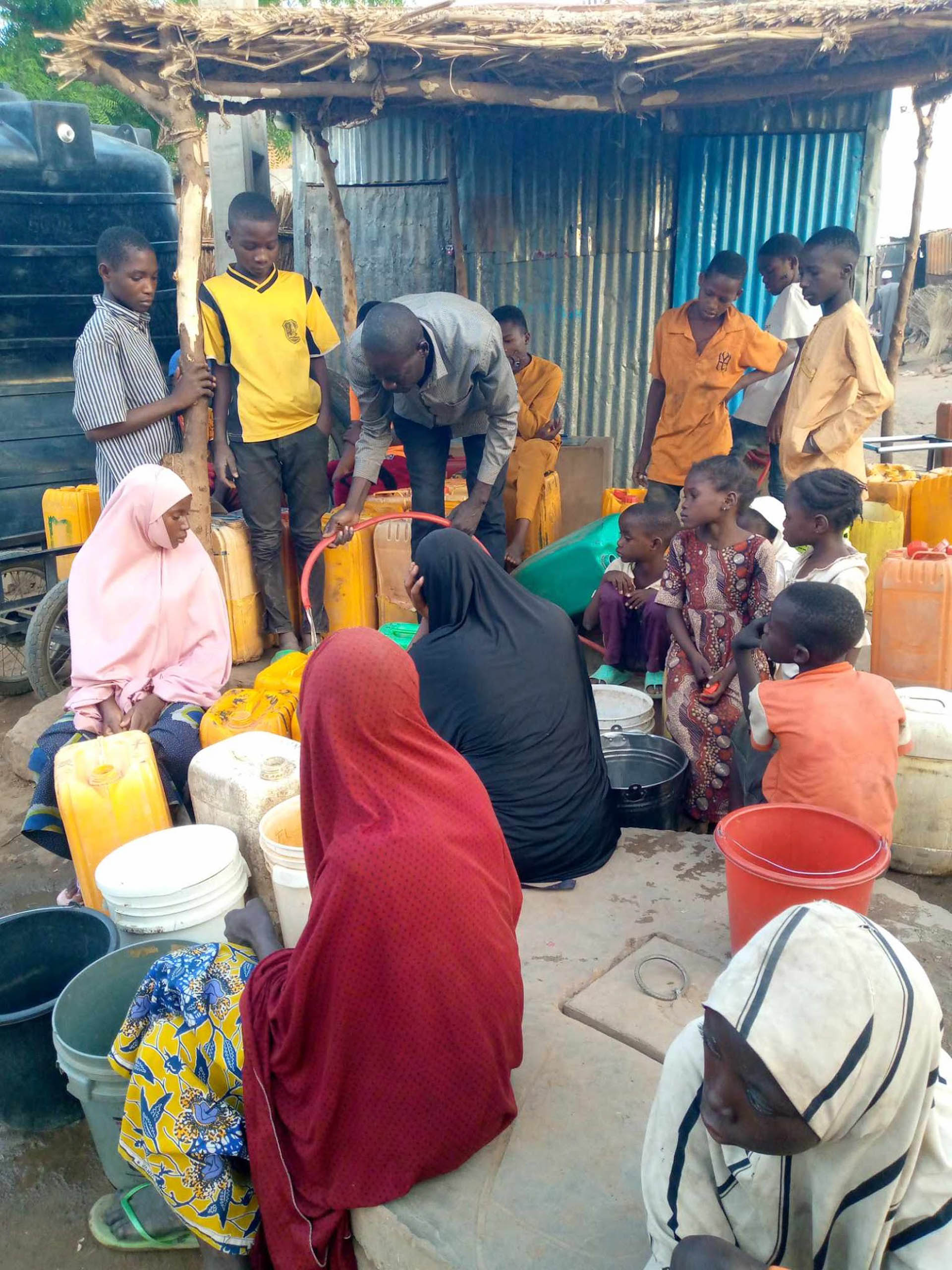 Mourtala Issa fuellt mit einem Schlauch die Kanister der Nachbarschaft bei der Wasserausgabe in Zinder, Niger