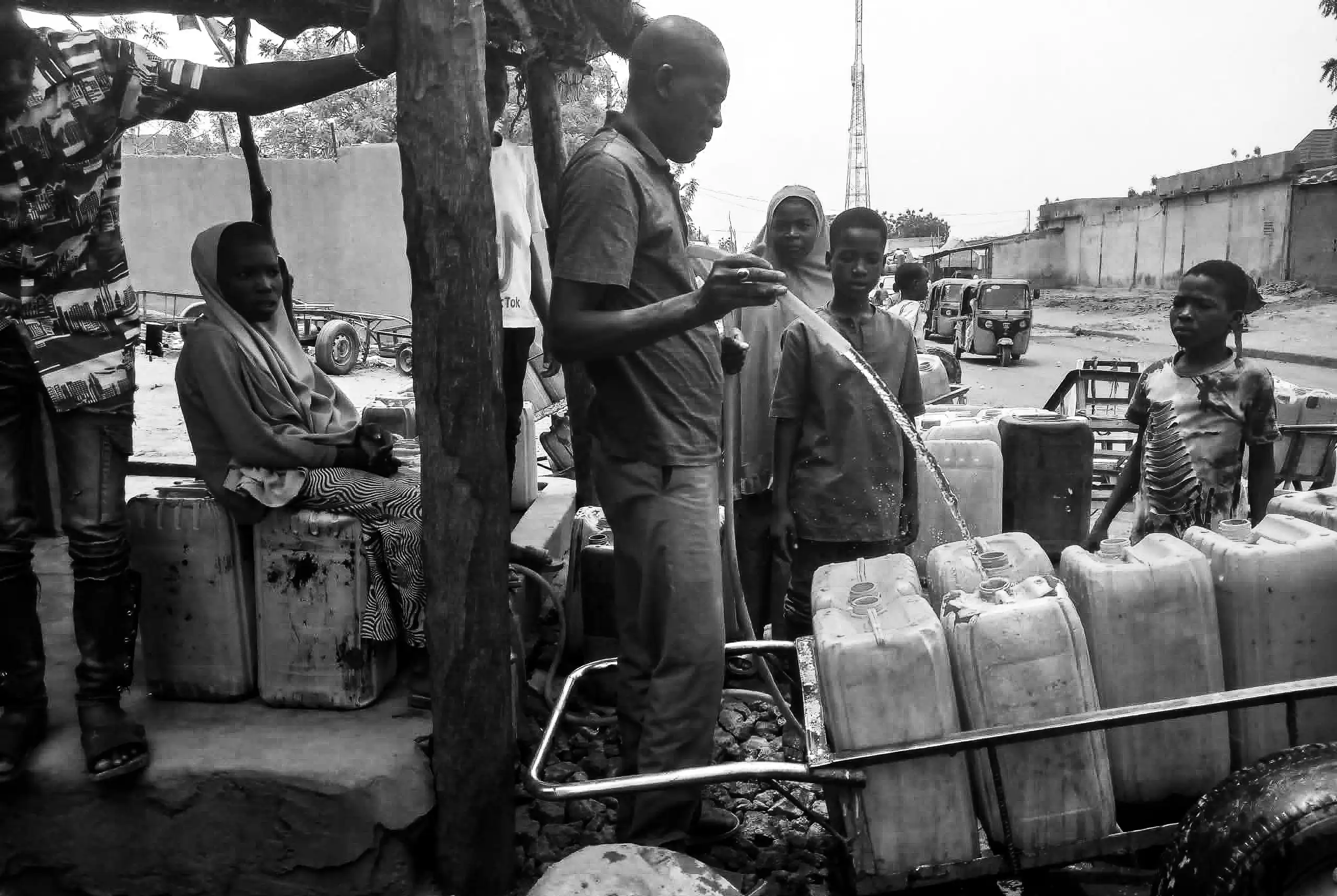 Wasserstelle in Zinder, Niger: Ein Mann füllt Kanister aus einem Schlauch, Kinder und Frauen warten mit Handkarren